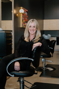 Headshot of salon owner, hair stylist, and hair colorist Cris sitting in salon chair.