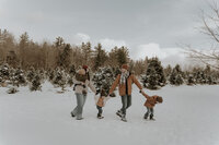 Family of five walking through a tree farm in Maine during a winter family photoshoot, cozy and candid New England family photography capturing joyful outdoor moments.