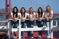 Five women posing on a fence dressed in white t-shirts and bluejeans in front of the golden gate bridge