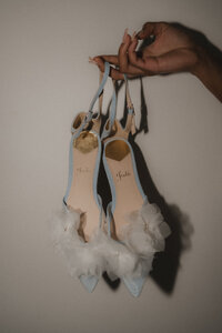Détail des souliers de mariée bleu pâle ornés de fleurs en tulle, suspendus par leurs brides, préparatifs de mariage au Four Seasons Montréal