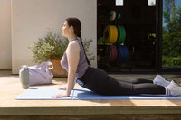Woman moving through a stretch on a mat outside the home gym