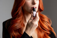 Close-up of woman with long red hair applying lipstick, photographed in studio. Photograph by Yucaipa branding photographer Kaitlyn Dawn Photography.
