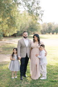 The Dilorio family posing together in a sunlit park, with parents and their two children smiling during a natural light outdoor family photography session in Las Vegas.