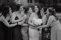 Mariée souriante entourée de ses demoiselles d'honneur, rires et étreintes complices, bouquet blanc en main, portrait de groupe au Vieux-Port de Montréal