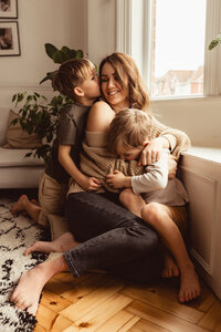 Carley sits on the floor with her children wrapped around her on in her lap and on from behind