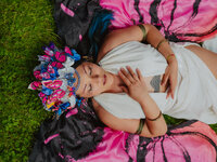 Artist lying outdoors in a colorful butterfly-inspired headpiece during a creative brand photoshoot