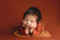 Baby boy posed safely on a burnt orange backdrop during his newborn photography session in South Central Minnesota.