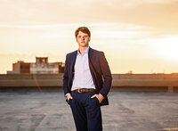 Senior portrait in downtown Mobile, Alabama— hands in pocket of his blue dress suit with sunset shining in the background.