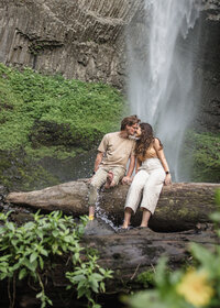 Couple sitting on log in front of latourell falls kissing