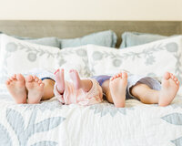 Close-up of two brothers and newborn baby sister lined up on a bed showing their feet side by side during an in-home family session.
