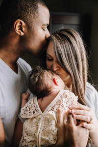 A man kisses his wife who kisses her newborn baby.