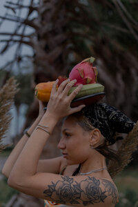 A jewelry model with tattoos and a bandana poses with a plate of fruit resting on her head in Galveston Texas