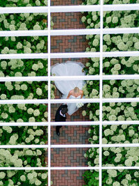 Editorial aerial view of a bride and groom standing on a brick path surrounded by lush white hydrangeas at Wychmere Beach Club.