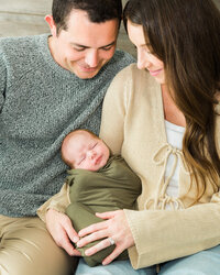 Mother and father looking down at their sleeping swaddled newborn during an in-home lifestyle newborn session.