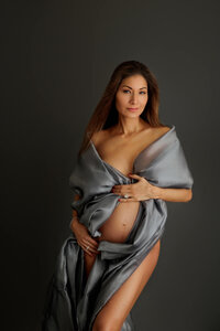 pregnant woman wrapped in dark gray fabric during fine art maternity portrait session in North Hollywood, dark moody setting