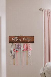 A name plate hangs on a wall in a nursery. It holds hair ties and bows.