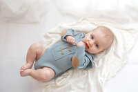 Six month old baby boy wearing a blue romper during his milestone session.