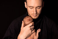 A dad holds his naked newborn against his shoulder.