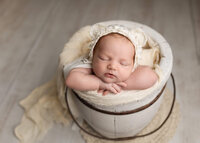 Baby girl safely posed in a wooden bucket during her newborn photoshoot with Jennifer Brandes Photography.