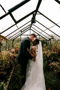 Elopement photographer captures newlyweds sharing a loving moment in a small greenhouse captured by colourful wedding photographher