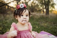 A one year old has cake and icing on her face from a cake smash photo session for her one year old birthday.