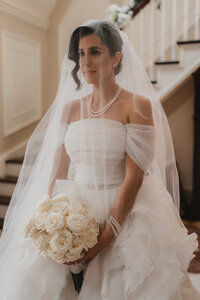 Portrait élégant d’une mariée dans la maison principale, bouquet de roses blanches à la main, voile délicatement posé, capturé par un photographe de mariage à Montréal — instant intemporel et poétique avant la cérémonie.