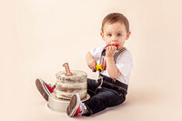 one year old sitting beside birthday cake holding small toy car by new bern milestone photographer