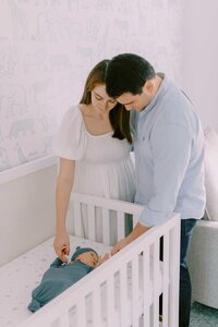 Baby laying in crib while parents hold both of his hands