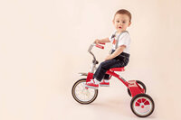 one year old riding red tricycle in bright studio portrait session