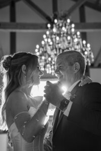 Couple smiling together during a romantic black and white wedding dance under chandeliers.
