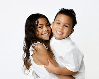 Two smiling siblings hugging during a studio children’s portrait session with Kaitlyn Dawn Photography at Yucaipa.