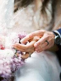 close-up of bride and groom holding hands with soft pink bouquet and delicate floral textures