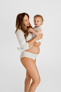 mother-to-be in neutral tones posing with her older child during timeless studio maternity session