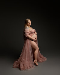 Expecting mother sitting in a flowing maternity gown during a studio maternity portrait by Kaitlyn Dawn Photography.