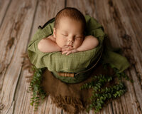 Sleeping newborn baby boy posed in a green bucket prop with hands under chin on a rustic wooden backdrop during a newborn photography session by Yucaipa newborn photographer Kaitlyn Dawn Photography.