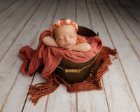 Newborn baby posed in a rustic wood bowl with warm rust and cream textures. Photographed by Inland Empire newborn photographer Kaitlyn Dawn Photography.