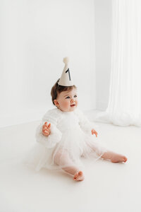 Baby girl with a birthday hat on during her first birthday photoshoot