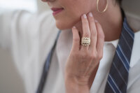 Close detail of a woman's hand resting near her chin, a large ring in focus against a white shirt and striped tie.