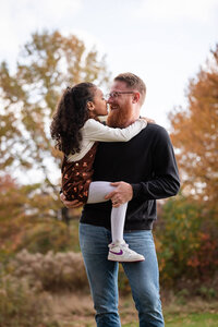 Father kissing his daughter's forehead while holding her in an autumn park during a Cleveland family photography session