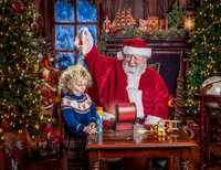 Young child watching Christmas magic sparkle around him while visiting Santa during a Santa’s Magical Christmas photography session in Jacksonville, Florida with Nature’s Child Photography, surrounded by glowing holiday lights, vintage toys, and cozy North Pole decor.