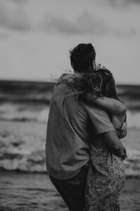 Black-and-white photo of a couple embracing from behind on the beach
