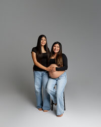 Pregnant woman posing with her daughter while seated, both smiling and holding her baby bump during an Inland Empire maternity session by Kaitlyn Dawn Photography.