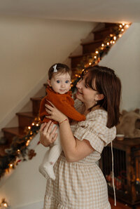 A mother cradles her baby while wearing a red dress in a New England home. Fine art lifestyle family photography capturing tender, intimate, and heartfelt parent-child moments.