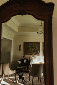 bride and groom posing in the bridal suite. bride sitting on the back of the couch and groom sitting on the seat of the couch touching fingers.
