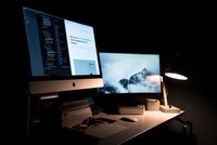 Computers on a desk in a dark room.