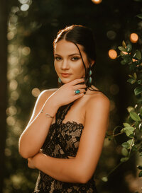 Senior portrait at Triple T Farms in Fruitdale, Alabama — black lace dress with greenery and
bokeh lights in the background.
