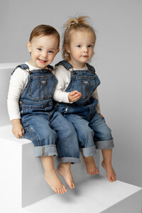 Two toddlers sitting together on white studio blocks in matching denim outfits, classic sibling portrait by Kaitlyn Dawn Photography, Inland Empire studio family photography.