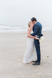 The couple shares a romantic kiss, their bare feet sinking into the damp sand.