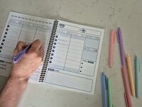 Hand writing inside the Time Magic Planner during a weekly planning session with colorful pens.