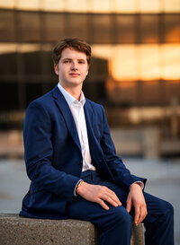 Senior portrait in downtown Mobile, Alabama— sitting on a cement barrier with a mirrored black building reflecting the golden sunset.